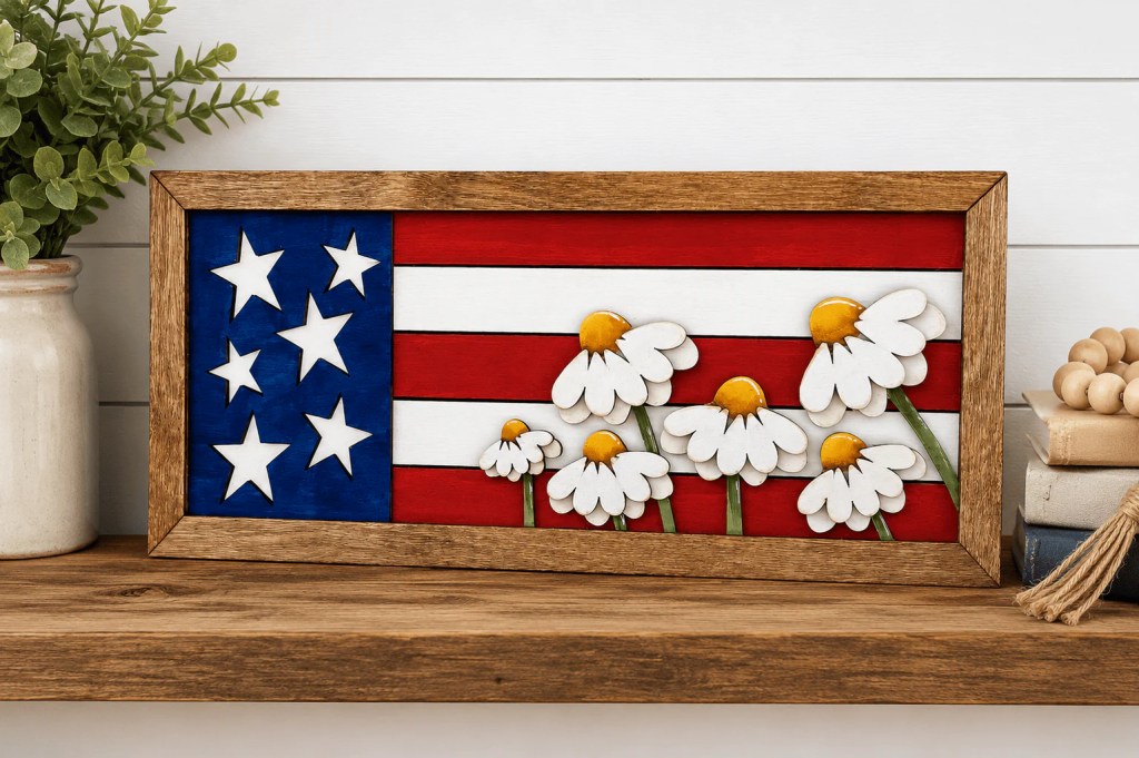 "Finished WallCutz Daisy Flag Frame Kit painted in red, white, blue, and yellow with hand-painted daisies, displayed on a wooden shelf"
