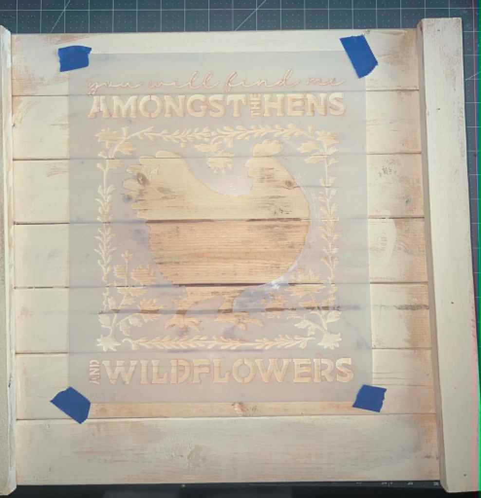 Two-layer hen stencil positioned on a prepped wood board before painting