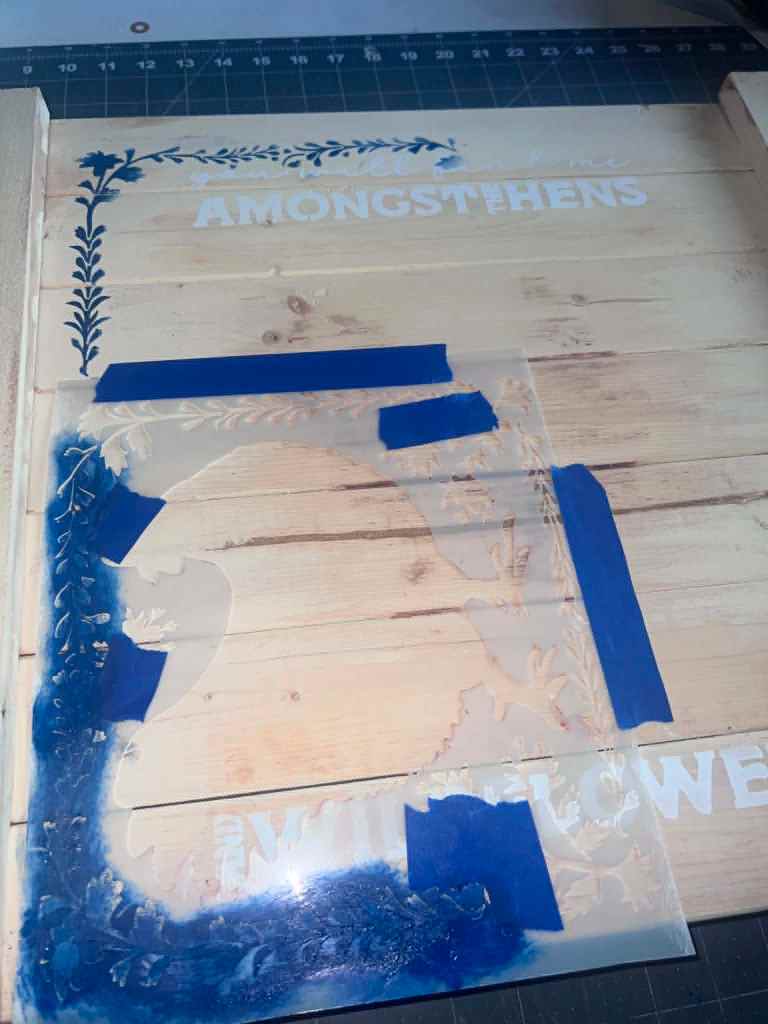 Navy floral vine border and white lettering being stenciled onto the board 